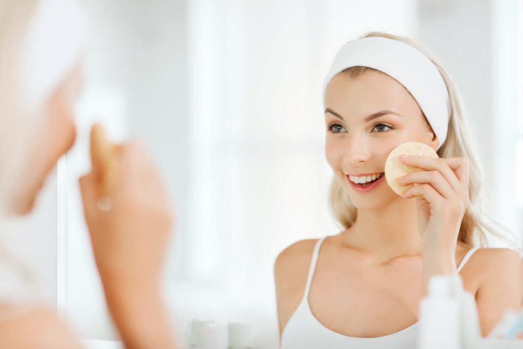 a young woman using a gentle exfoliator on the face while looking at the mirror