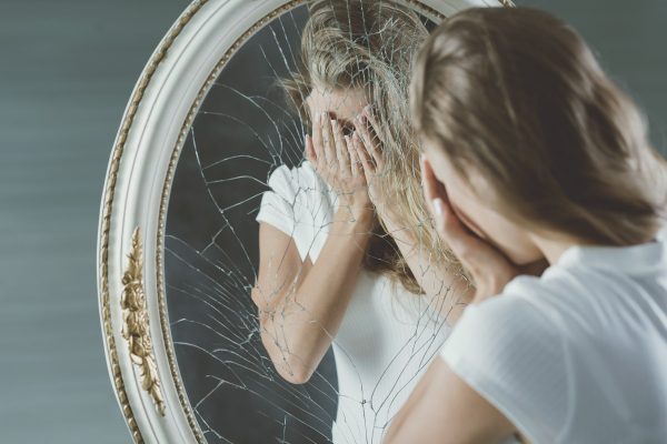 a crying woman in front of a broken mirror