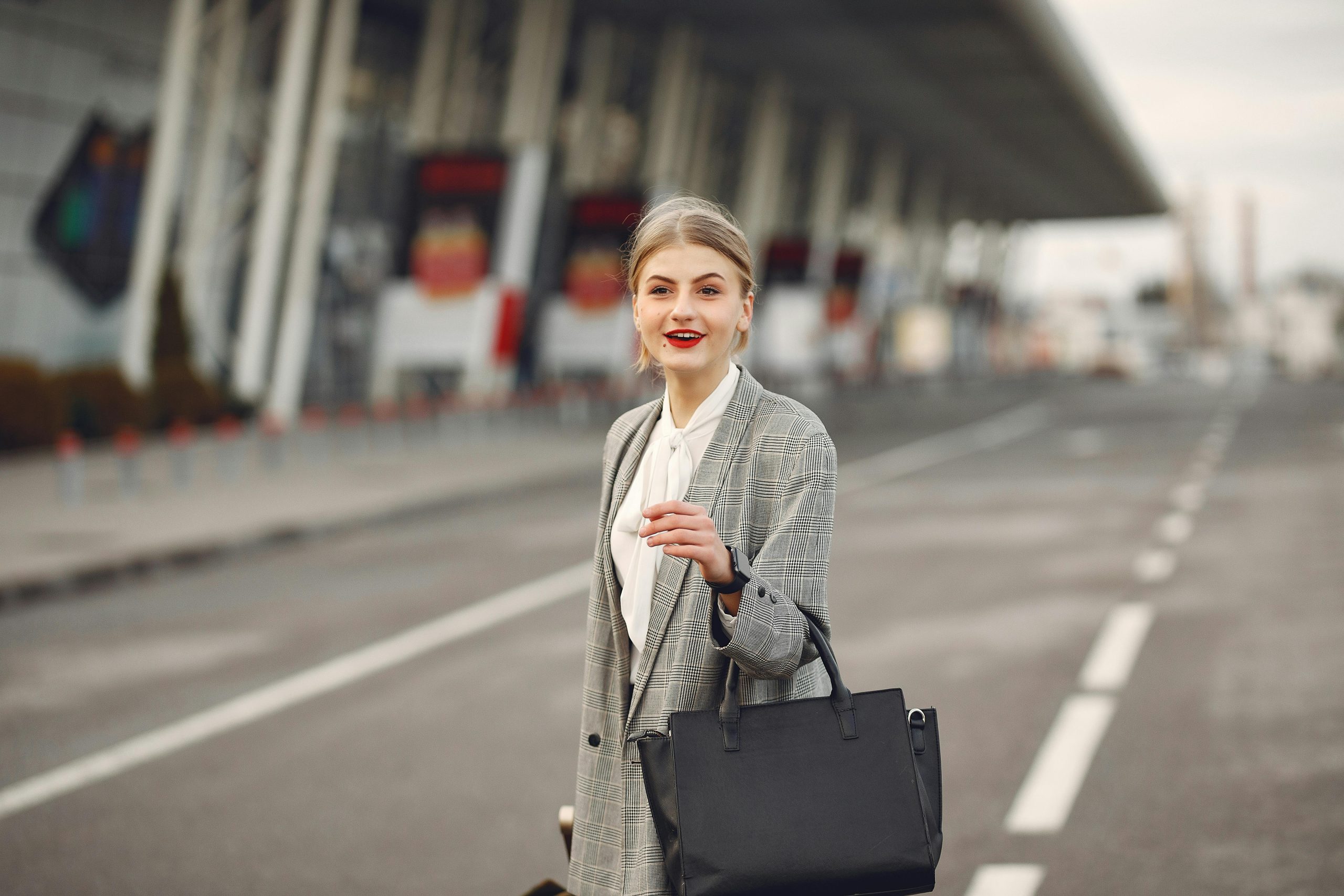 woman wearing a gray coat over a white top, with a black handbag dangling from her arm